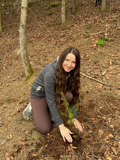 Sophia Janker kniet auf dem Boden und pflanzt einen Baumsetzling.